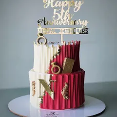 A two-tiered cake for a corporate 5th-anniversary celebration for Nirmal Jewellers. This design features a modern origami-style texture in red and white, accented with gold rings and the company's initial.