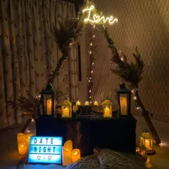 For a cozy and personal evening, I created this intimate date night setting. It features a boho-style teepee frame, warm candlelight from lanterns, a custom 'Love' neon sign, and comfortable floor seating with macrame pillows, perfect for a private celebration at home.