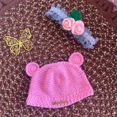 This image shows the pink bear-ear beanie next to a delicate crochet flower headband. Both are handmade and make a beautiful gift set for a baby.