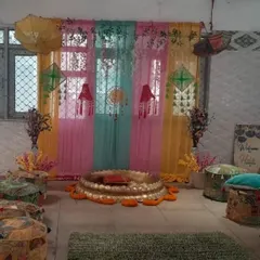 A cozy indoor setup for a Haldi or Mehendi ceremony, showing how we arrange guest seating with traditional poufs. The decor includes a decorated urli and a colorful window backdrop.