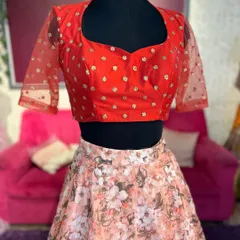 A bright red blouse with sheer, dotted sleeves paired with a light pink floral skirt. This mannequin shot shows a vibrant lehenga option.
