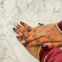 A close-up of a festive nail art design, combining a deep maroon polish with gold glitter accents. This look is perfect for bridal or party occasions.