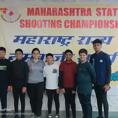 A coach stands proudly with his team of young male shooters at the Maharashtra State Shooting Championship. My coaches are partners in our athletes' journeys, present at every competition.