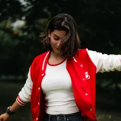 A candid, joyful shot of a model in a red and white varsity jacket, captured mid-motion. This style of image shows personality and is great for lifestyle or commercial work.