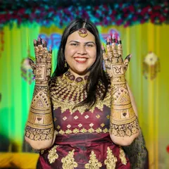 A beautiful bride proudly displaying her full-arm bridal mehendi. The design includes her and her partner's initials, 'AR', and a special message.
