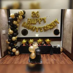 A classic and elegant 26th-anniversary decoration. This setup features a black and gold theme with a balloon garland and large 'Happy Anniversary' foil letters.