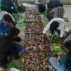 A wide view of a busy workshop in full swing. With trays full of LEGOs stretching across the floor, kids and adults get completely absorbed in the creative process.