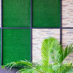 A custom vertical garden design featuring panels of artificial turf set within a sleek black metal frame against a textured stone wall. This image highlights how I combine different materials to create unique and stylish accent walls for both indoor and outdoor spaces.