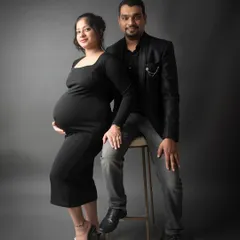 A classic and elegant studio portrait of an expecting couple. Dressed in black against a simple grey background, their connection and excitement are the main focus.