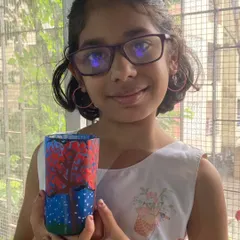 Spruha, a 4th standard student, shows off her glass painting. She has painted a beautiful seasonal tree on a glass, learning how to use special paints for a transparent effect.