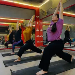 Students holding Virabhadrasana I (Warrior I Pose) in a group class. This pose builds strength in the legs and opens the chest.