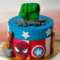 An epic Avengers-themed cake for a superhero fan. This design includes the Hulk's fist smashing through the top, Captain America's shield, Thor's hammer, and Spider-Man's mask, all handcrafted in fondant.