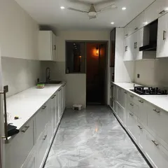 A full view of the parallel kitchen layout, which allows for an efficient work triangle between the stove, sink, and refrigerator. The grey marble-finish floor complements the white cabinetry.