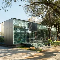 The completed VPG Experience Center in Bangalore. The minimalist glass box, set in a green landscape, creates a calm and welcoming environment for prospective home buyers.