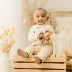 An adorable portrait of a baby boy sitting on a wooden crate, holding a toy airplane. The soft, neutral tones of the studio and his outfit create a timeless look.
