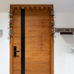 A simple yet charming entryway with a modern wooden door. The traditional 'toran' with colorful figurines adds a delightful and personal desi touch.