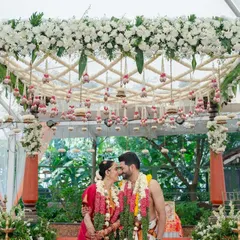 We believe in creating picture-perfect moments. Here, the couple shares a quiet moment under a custom-designed mandap, rich with fresh white orchids and traditional hanging bells, embodying the blend of intimacy and grandeur we strive for in our South Indian wedding designs.