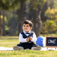 A magical moment captured outdoors, with bubbles floating around a smiling birthday boy dressed in a smart vest and bow tie.