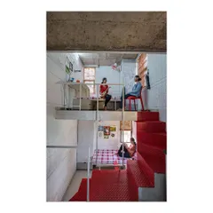 The interior of a room in our 'Stacked Student Housing' project, showing how a split-level design maximizes space. The lofted study area and lower sleeping zone create distinct functional areas within a compact footprint, connected by a bold red steel staircase.