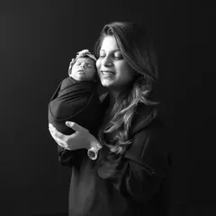 A mother's warm smile as she holds her swaddled newborn close. This black and white image highlights the tender bond between mother and child, using simple lighting to draw attention to emotion.