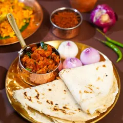 A rustic platter featuring freshly made bhakri served with a spicy shrimp preparation, whole onions, and green chilies. This shot captures the essence of a simple yet flavorful Maharashtrian meal.
