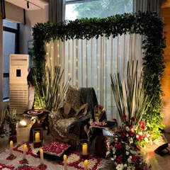An angled view of a satsang setup, highlighting the depth and layers of the decoration. The combination of fresh flowers, green accents, and warm candlelight creates a truly blessed environment.