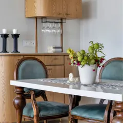 This dining area features a sophisticated bar cabinet, perfect for entertaining. The classic wooden chairs with teal velvet upholstery add a touch of vintage glamour, while the modern bar unit provides practical storage.