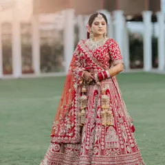 A stunning full-length portrait of a bride in her traditional red lehenga, captured outdoors to showcase the intricate embroidery and her complete bridal look.