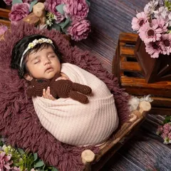 This is a wider view of a floral-themed setup, showing how I use props like a miniature wooden bed and crates of flowers to build a beautiful scene. The baby is kept safe and comfortable while I create this artful portrait.