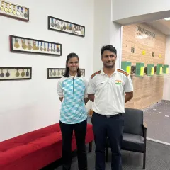 A coach and student stand in front of our wall of medals. This represents the journey every shooter, from beginner to champion, embarks on with us.