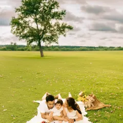 A beautiful aerial view of a family enjoying a picnic in a vast green meadow. This composition emphasizes their closeness and the peaceful, idyllic setting of their outdoor family photoshoot.