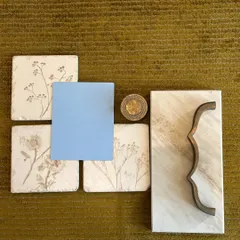 A mood board exploring a gentle contrast of materials. The delicate floral tiles, a pop of sky blue, and a uniquely curved metal handle against a marble slab are the beginning of a kitchen with a soft, artistic personality.