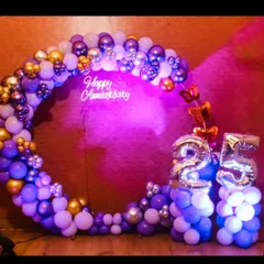 A beautiful 25th anniversary decoration with a purple and gold balloon circle. The setup includes a "Happy Anniversary" neon sign and large silver foil number balloons.