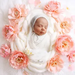 A delicate newborn portrait showing a baby nestled in soft white wraps, encircled by beautiful pink peonies. We focus on creating serene and timeless images, paying close attention to every soft detail.