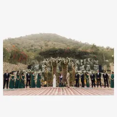 A wide shot of a beautiful outdoor vow ceremony, with the wedding party flanking the couple. Set against the Aravalli mountains, this image showcases the scale and beauty of a destination wedding ceremony.