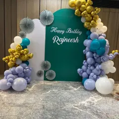 A sophisticated and personalized 50th birthday backdrop. We used custom arched panels in white and deep green, adorned with an organic balloon garland in lavender, teal, and chrome gold for a unique and modern celebration.