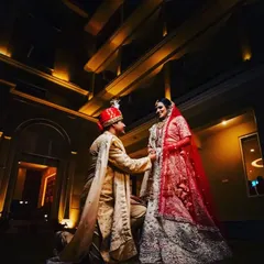 A classic wedding portrait where the groom is on one knee, captured against a beautifully lit venue at night.