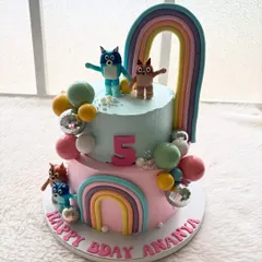 A colorful two-tier Bluey-themed cake for a 5th birthday party. It features handcrafted characters, rainbows, and fun disco balls to bring the cheerful world of Bluey and Bingo to life.