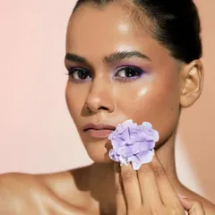 A powerful portrait where the model holds the flower. The vibrant purple on the eyes stands out beautifully against her glowing skin.