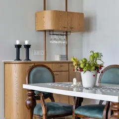 This dining area features a sophisticated bar cabinet, perfect for entertaining. The classic wooden chairs with teal velvet upholstery add a touch of vintage glamour, while the modern bar unit provides practical storage.