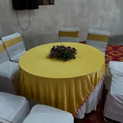 A simple and clean seating arrangement with a yellow tablecloth and white chair covers with gold sashes, ideal for Haldi or Mehendi functions.