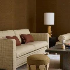 A serene living room where our Nobilis fabrics create a grounded, elegant atmosphere. The sofa and ottoman are upholstered in tactile, earthy-toned textiles that coordinate beautifully with the textured brown wallcovering.