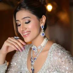 A close-up on this stunning cocktail look. The makeup features a shimmery, silver-toned eyeshadow with a pop of blue from the jewelry, creating a bold and beautiful statement.