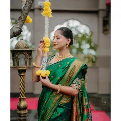 A graceful pose with traditional flower decorations. The bride's emerald green saree and gold jewelry shine in this elegant solo shot.