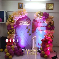 A chic first birthday setup using trendy arched backdrops and a beautiful arrangement of magenta and gold balloons. This decor fits perfectly against a wall in your home.