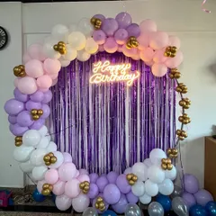 A simple yet beautiful balloon ring decoration for a birthday. This setup uses a purple foil curtain as a backdrop and a balloon arch in pastel shades of purple, pink, and white with gold accents.