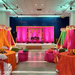 A colorful Mehendi setup with bright drapes in orange, pink, and green. The decor includes a traditional jhoola on the stage and low seating with bandhani print cushions for a festive feel.