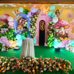 An enchanted forest theme for a 5th birthday party. The stage is decorated with magical mushroom props, fairy cutouts, and a lush arrangement of balloons and flowers, creating a storybook setting.