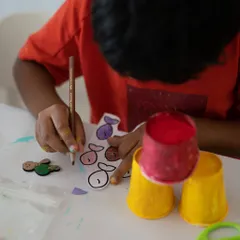 The start of a mixed-media masterpiece. Here, a child is carefully coloring fish cutouts that will become part of a larger 3D underwater scene. We use simple materials to create magical results.