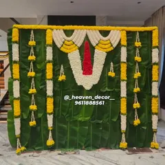 This backdrop is a tribute to South Indian tradition, crafted for a sacred ceremony. We used a full wall of fresh banana leaves, accented with garlands of jasmine and marigold, and a central floral 'Namam' to create an authentic and divine atmosphere.